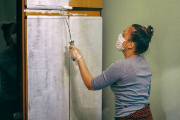 Women wearing a protective mask upcycling a wooden wardrobe by painting it white with a paint roller