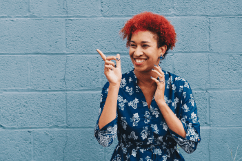 Young woman smiling and pointing in front of a blue wall