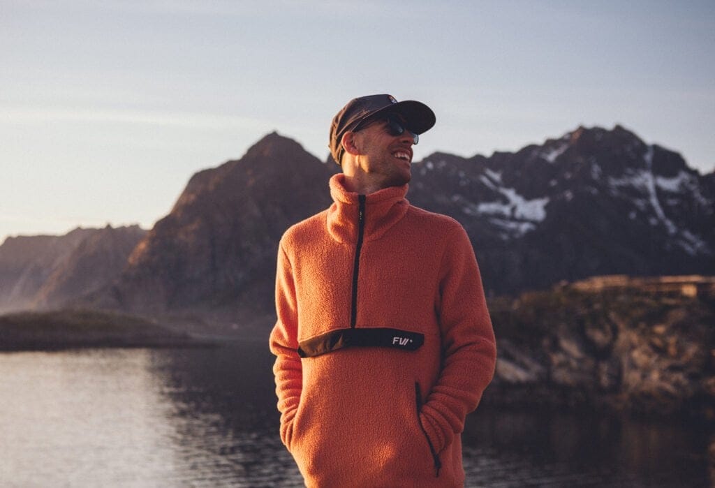 Man in orange fleece smiling in front of mountains