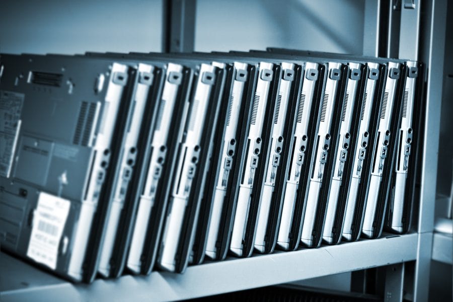 Refurbished silver laptops in a row on a metal shelf